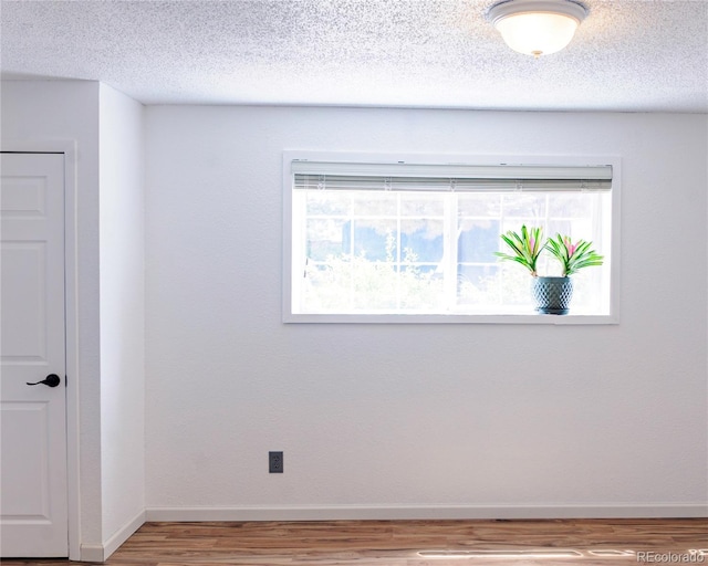 empty room featuring baseboards, a textured ceiling, and wood finished floors