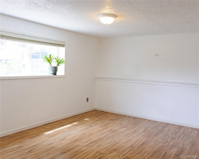 empty room with baseboards, a textured ceiling, and wood finished floors