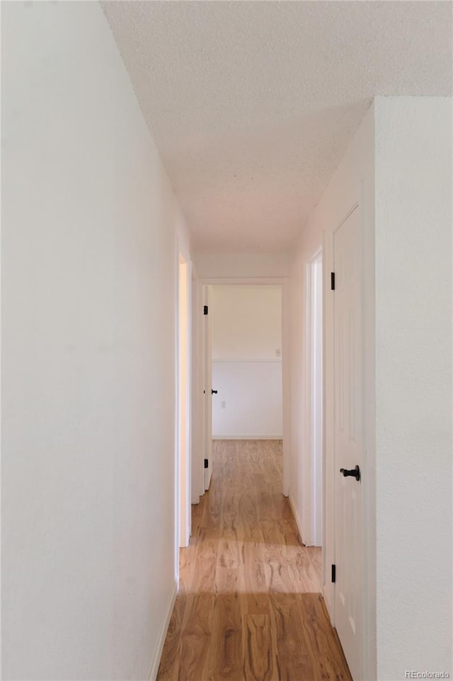 corridor featuring baseboards, light wood-style flooring, and a textured ceiling