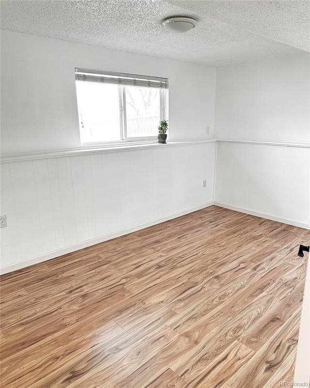 empty room featuring a textured ceiling, wainscoting, and wood finished floors