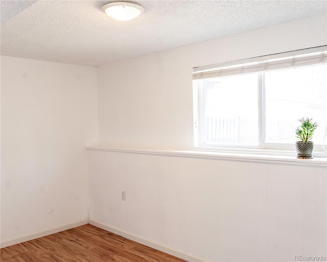 empty room with a textured ceiling, baseboards, and wood finished floors