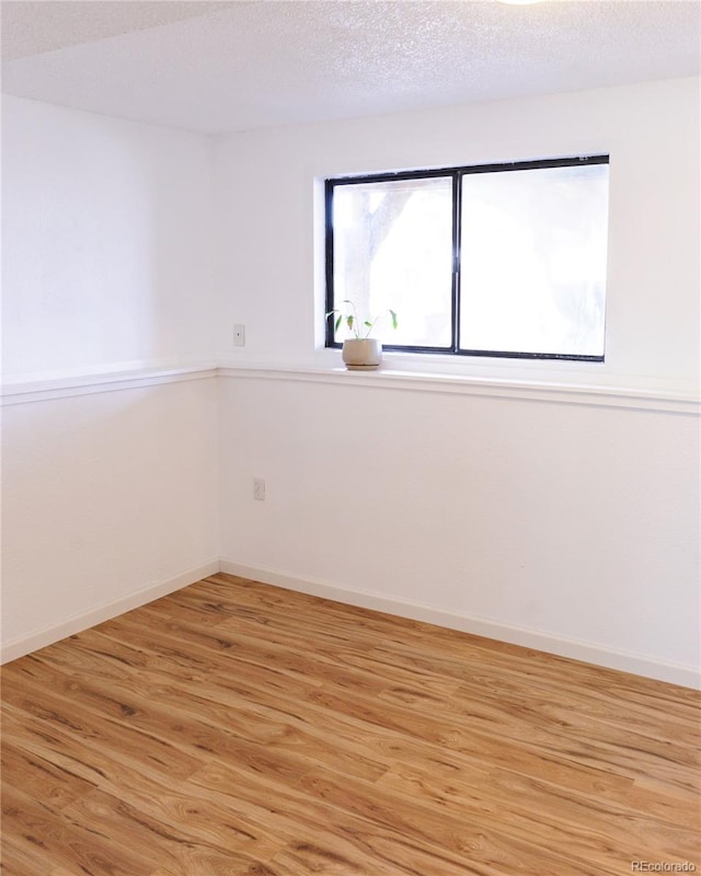 unfurnished room with light wood-style floors, a textured ceiling, and baseboards