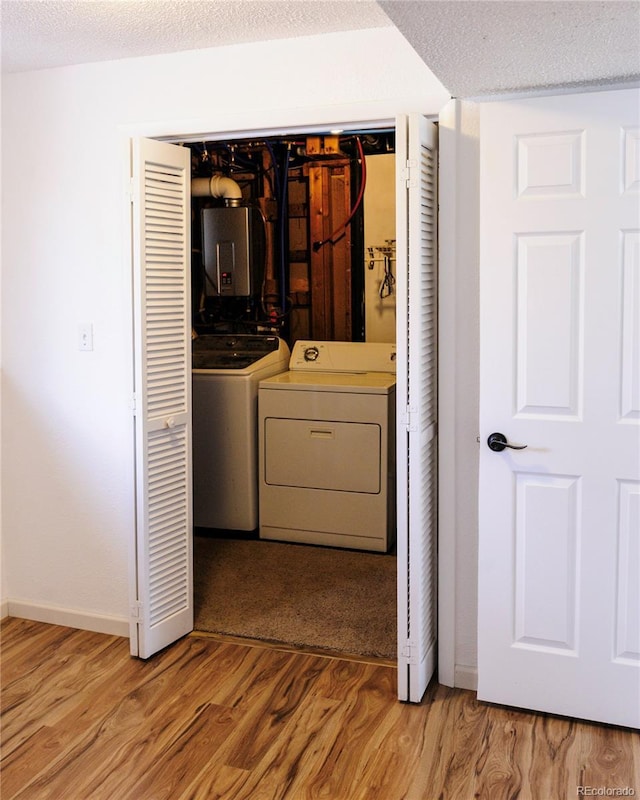 laundry area with a textured ceiling, light wood-style flooring, baseboards, washer and clothes dryer, and electric panel