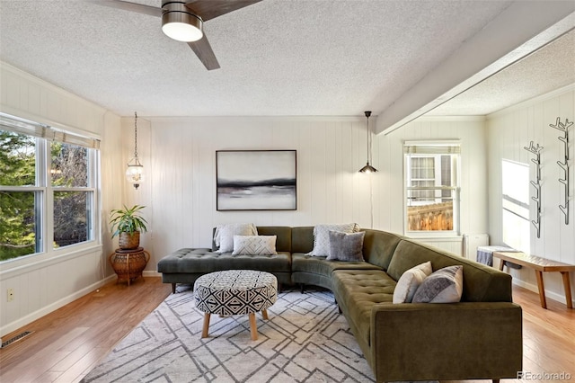 living room featuring a textured ceiling, light hardwood / wood-style flooring, ceiling fan, and wooden walls