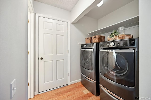 washroom with a textured ceiling, light hardwood / wood-style flooring, and washing machine and clothes dryer