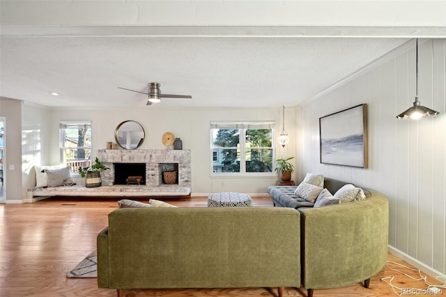 living room with ceiling fan, a brick fireplace, hardwood / wood-style floors, a textured ceiling, and ornamental molding