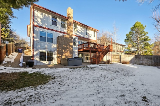 snow covered back of property featuring a wooden deck and a hot tub