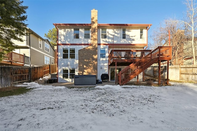 snow covered back of property featuring a jacuzzi and a deck