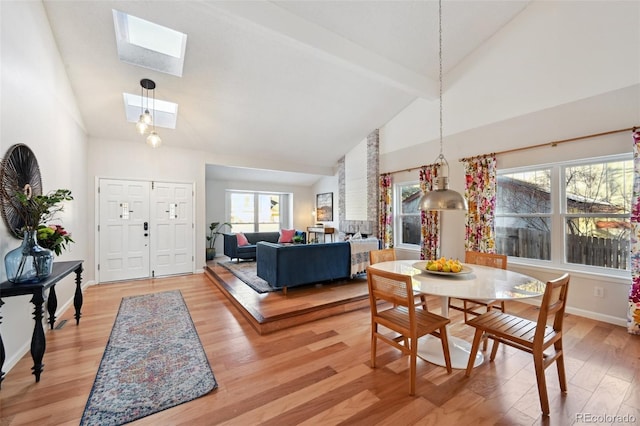 dining space with beam ceiling, a skylight, high vaulted ceiling, and hardwood / wood-style flooring