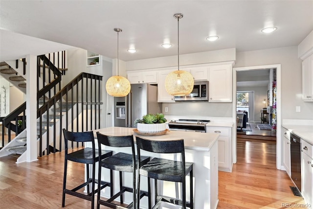 kitchen featuring pendant lighting, white cabinets, appliances with stainless steel finishes, and light hardwood / wood-style flooring