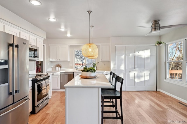 kitchen featuring ceiling fan, a center island, decorative light fixtures, white cabinets, and appliances with stainless steel finishes