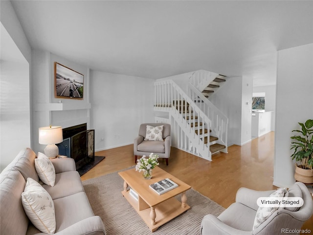 living room with stairs, baseboards, a fireplace with raised hearth, and wood finished floors