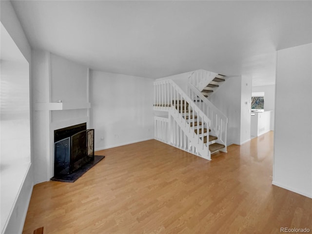 unfurnished living room featuring light wood-type flooring, baseboards, stairway, and a fireplace with raised hearth