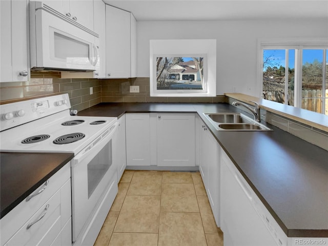 kitchen with light tile patterned floors, white appliances, a sink, backsplash, and dark countertops