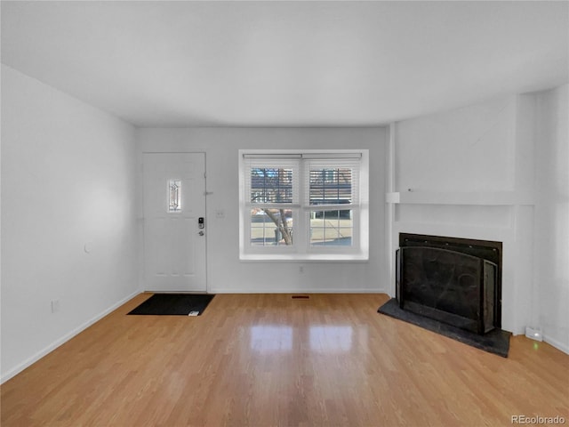 foyer with baseboards, a fireplace with raised hearth, and wood finished floors