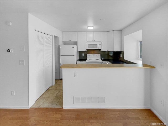 kitchen with white appliances, visible vents, white cabinets, a peninsula, and light wood-type flooring