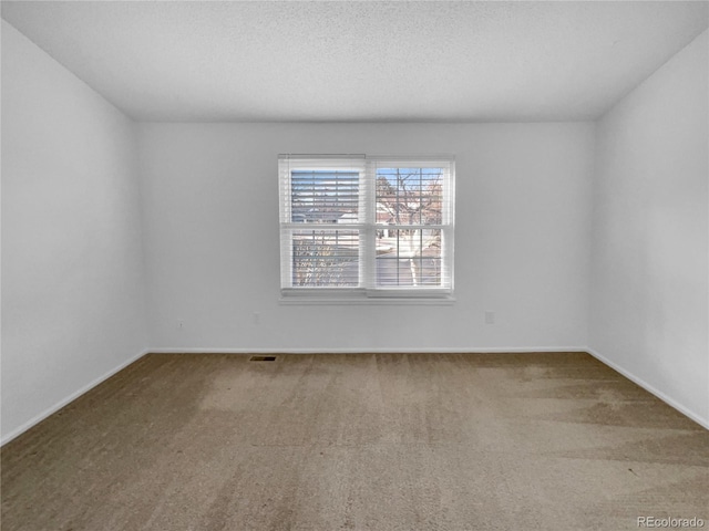 carpeted spare room featuring a textured ceiling and baseboards