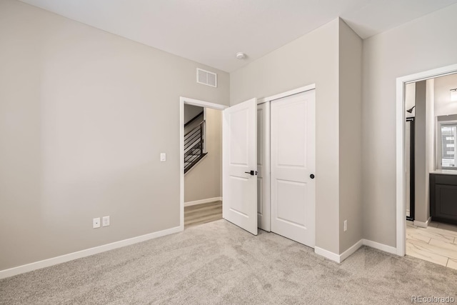 unfurnished bedroom with a closet, ensuite bath, and light carpet