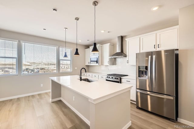 kitchen with sink, hanging light fixtures, stainless steel appliances, a center island with sink, and wall chimney exhaust hood