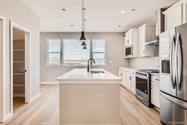 kitchen with appliances with stainless steel finishes, an island with sink, sink, white cabinets, and hanging light fixtures