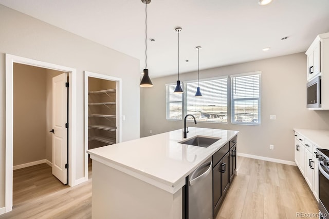 kitchen with sink, a kitchen island with sink, stainless steel appliances, white cabinets, and decorative light fixtures