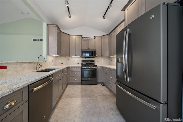 kitchen with vaulted ceiling, appliances with stainless steel finishes, sink, backsplash, and light stone counters