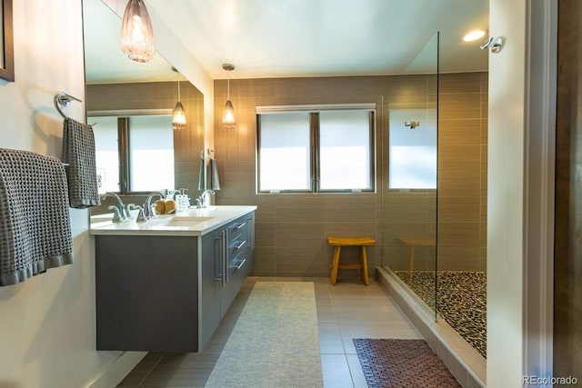 bathroom with tile patterned flooring, double vanity, tiled shower, tile walls, and a sink