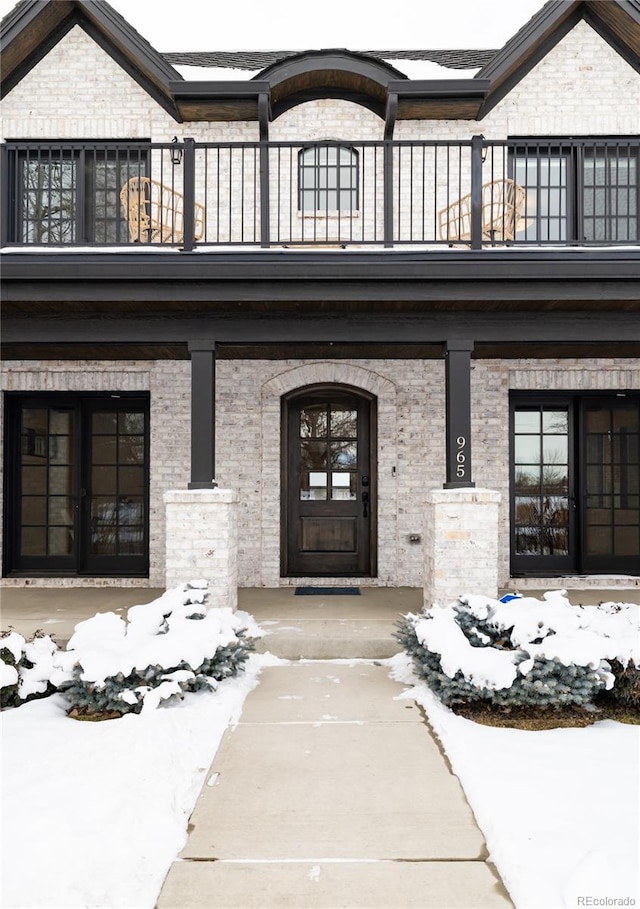 snow covered property entrance with a balcony