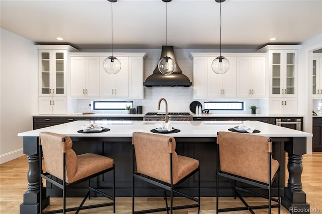 kitchen with white cabinetry, a center island with sink, custom range hood, and hanging light fixtures