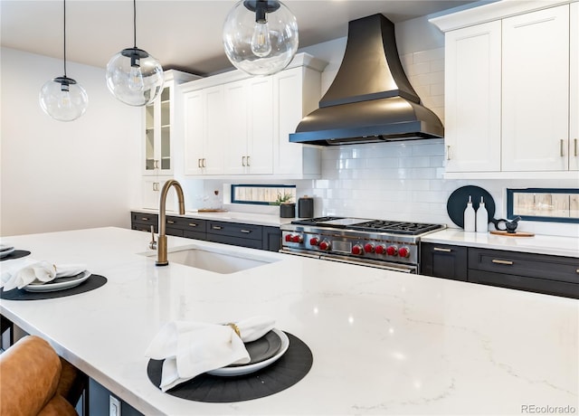 kitchen featuring decorative light fixtures, white cabinets, range hood, and stainless steel range