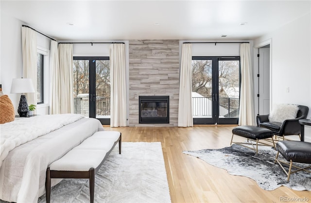 bedroom with light wood-type flooring, french doors, access to outside, and a tiled fireplace