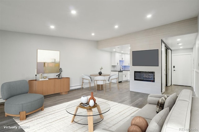 living room featuring sink, a large fireplace, a baseboard heating unit, and light hardwood / wood-style flooring