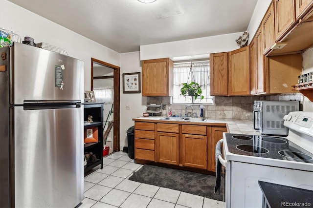 4940-42 W 9th Ave W, Denver, CO 80204 - kitchen with freestanding refrigerator, white electric range, tile counters, decorative backsplash, and brown cabinetry