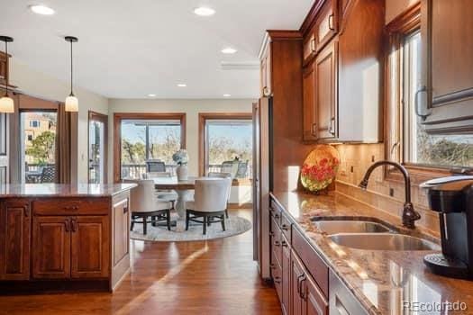 kitchen with light stone counters, dark wood-style flooring, brown cabinets, hanging light fixtures, and a sink