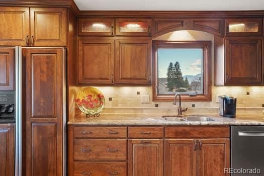 kitchen with a sink, light stone countertops, paneled built in refrigerator, and dishwasher