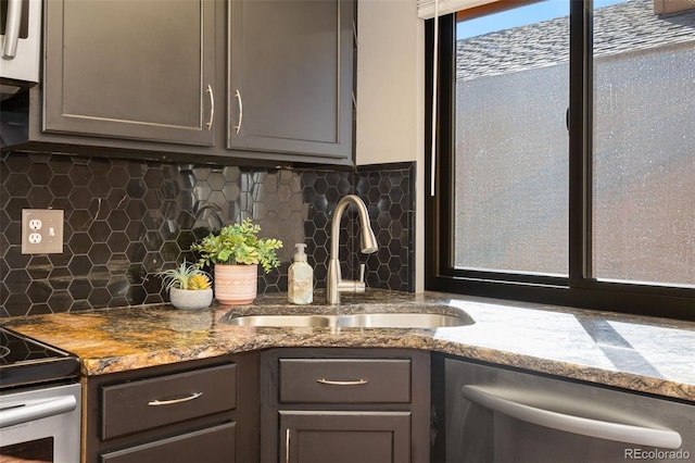 kitchen with light stone countertops, gray cabinets, a sink, stainless steel appliances, and backsplash