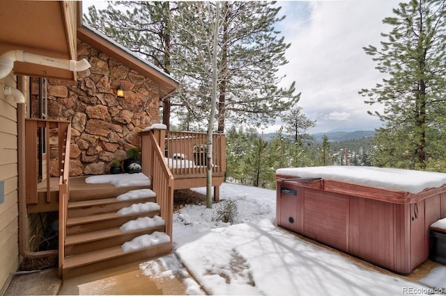 snowy yard featuring a hot tub, a deck with mountain view, a patio area, and stairway