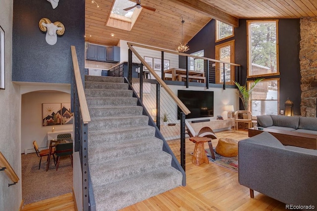 staircase with wooden ceiling, high vaulted ceiling, wood finished floors, a skylight, and a chandelier