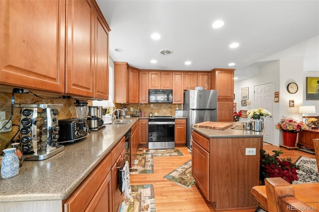 kitchen featuring a center island, backsplash, sink, light hardwood / wood-style flooring, and appliances with stainless steel finishes