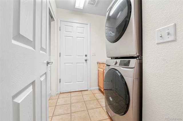 laundry area with cabinets, light tile patterned floors, and stacked washing maching and dryer