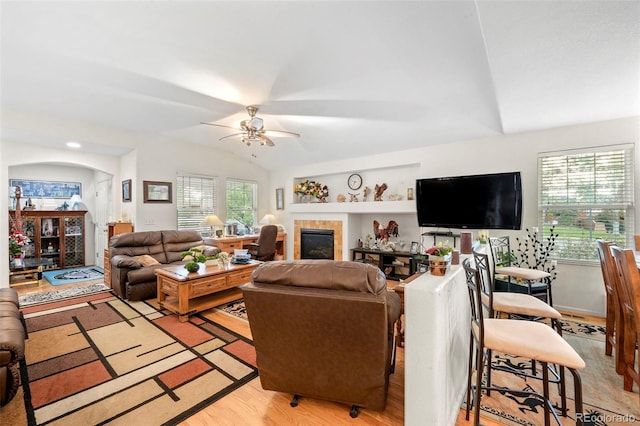 living room with a tile fireplace, vaulted ceiling, light hardwood / wood-style flooring, and ceiling fan