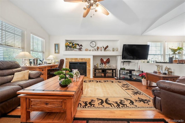 living room featuring ceiling fan, light hardwood / wood-style floors, a tile fireplace, and vaulted ceiling