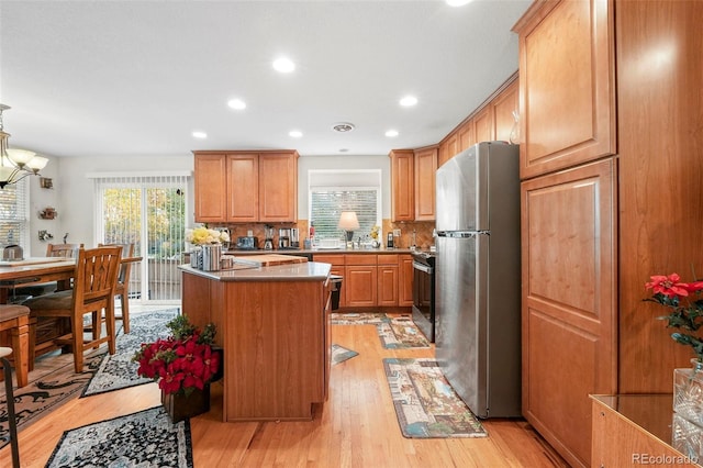 kitchen with appliances with stainless steel finishes, light wood-type flooring, tasteful backsplash, a center island, and hanging light fixtures