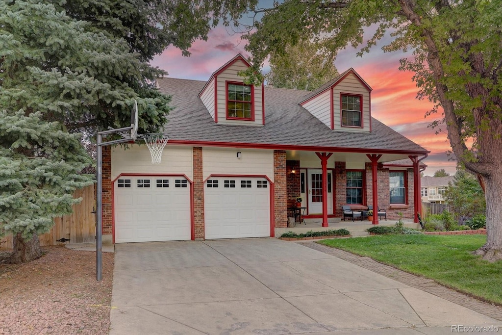 cape cod house featuring a garage, a yard, and a porch