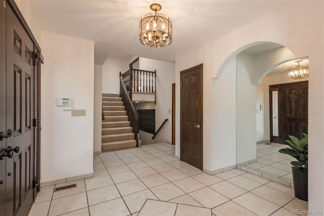 entrance foyer featuring visible vents, arched walkways, light tile patterned floors, a chandelier, and stairs