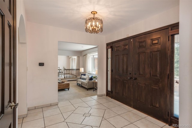 entrance foyer featuring an inviting chandelier, light tile patterned floors, light carpet, and a wealth of natural light
