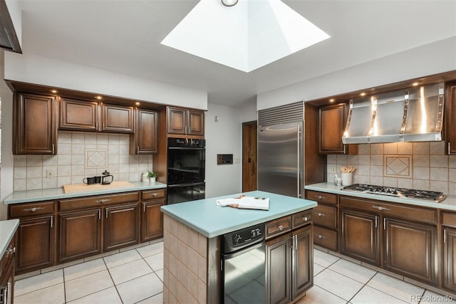 kitchen with wall chimney range hood, appliances with stainless steel finishes, light tile patterned floors, and tasteful backsplash