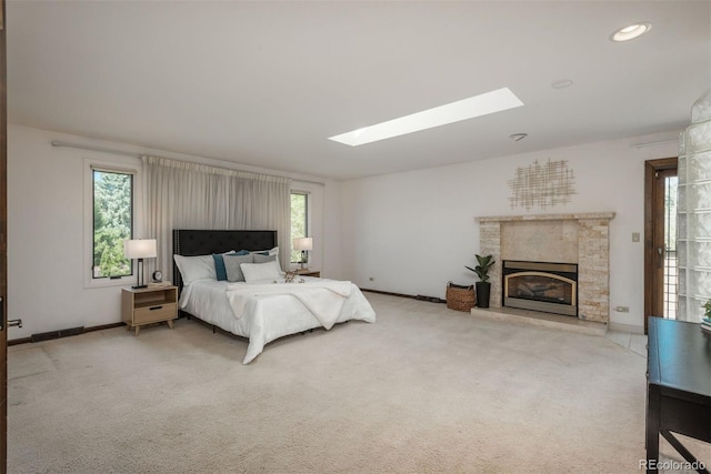 bedroom featuring baseboards, a glass covered fireplace, multiple windows, and a skylight