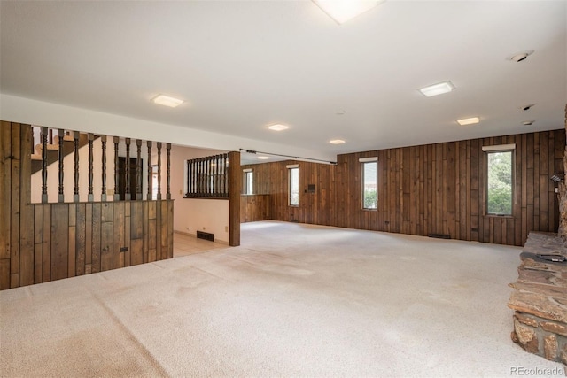unfurnished living room featuring a wealth of natural light, carpet, wood walls, and visible vents