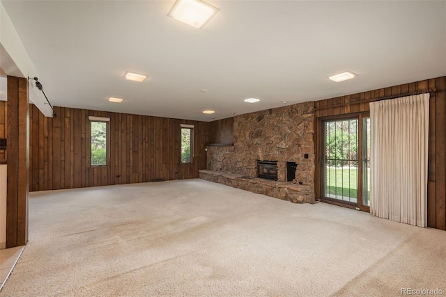 unfurnished living room featuring carpet flooring, wooden walls, a fireplace, and a healthy amount of sunlight